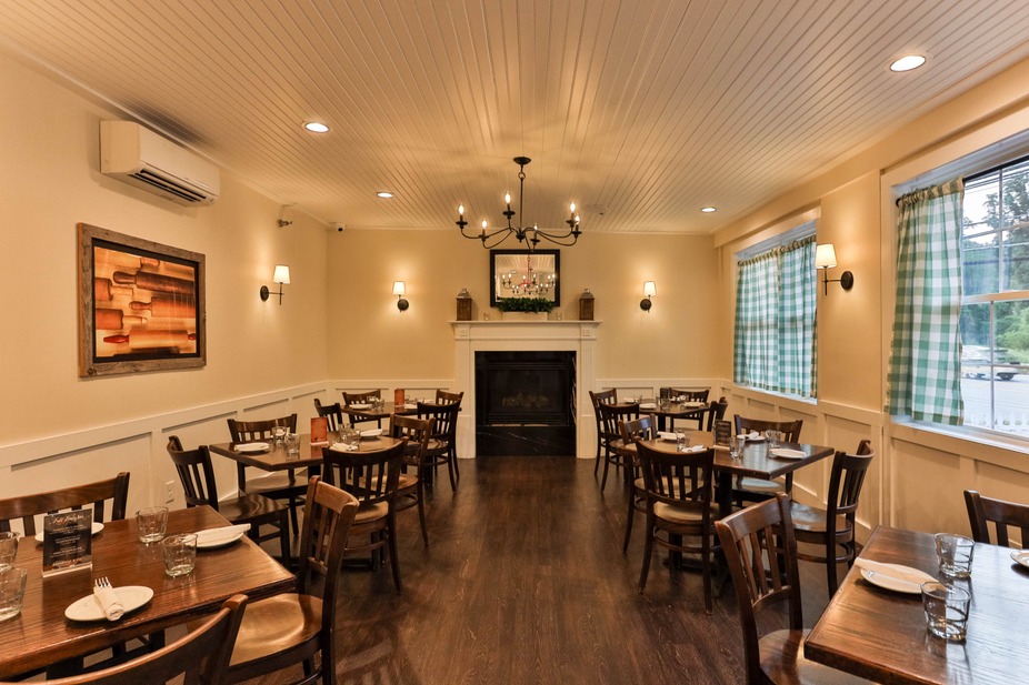 Restaurant dining room with tables, chairs, fireplace, and checkered curtains.