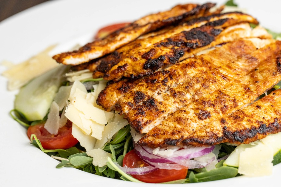 Grilled chicken salad with shaved cheese, tomatoes, and arugula.