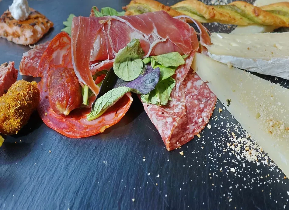 A charcuterie board with cured meats, cheeses, and a twisted pastry.