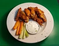 A white plate with chicken wings, carrots, celery, and dip.