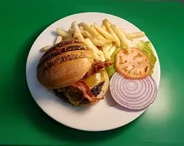 A cheeseburger with fries, onion slices, lettuce, and a tomato slice.