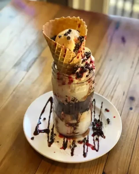 Dessert jar with ice cream cone, chocolate syrup, and berries on a plate.