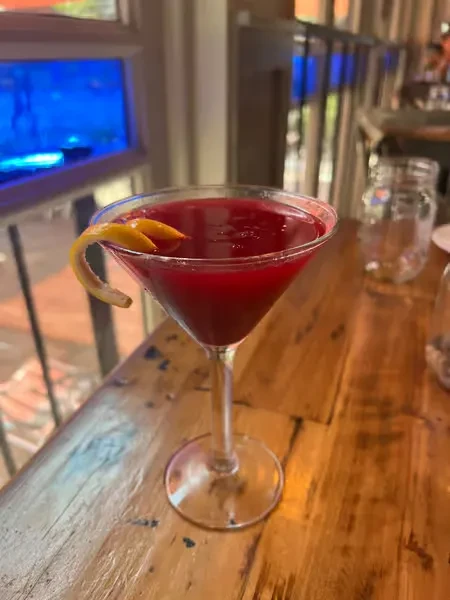 A red cocktail with a lemon twist on a wooden table.