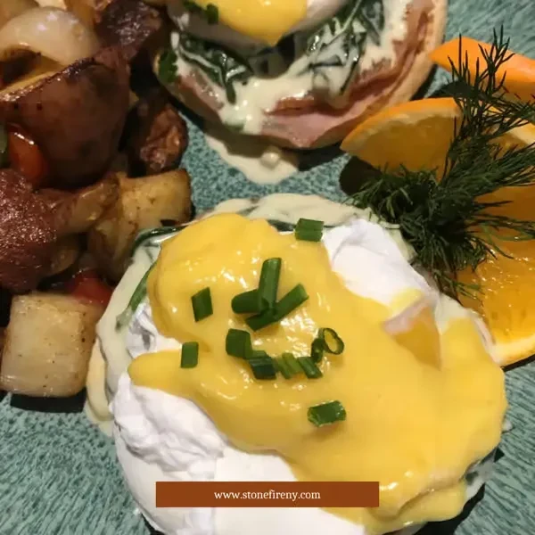 Eggs Benedict with home fries and orange slices on a teal plate.