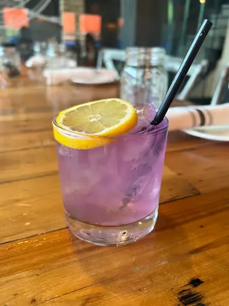 Close-up of a purple drink with a lemon slice and straw on a wooden table.