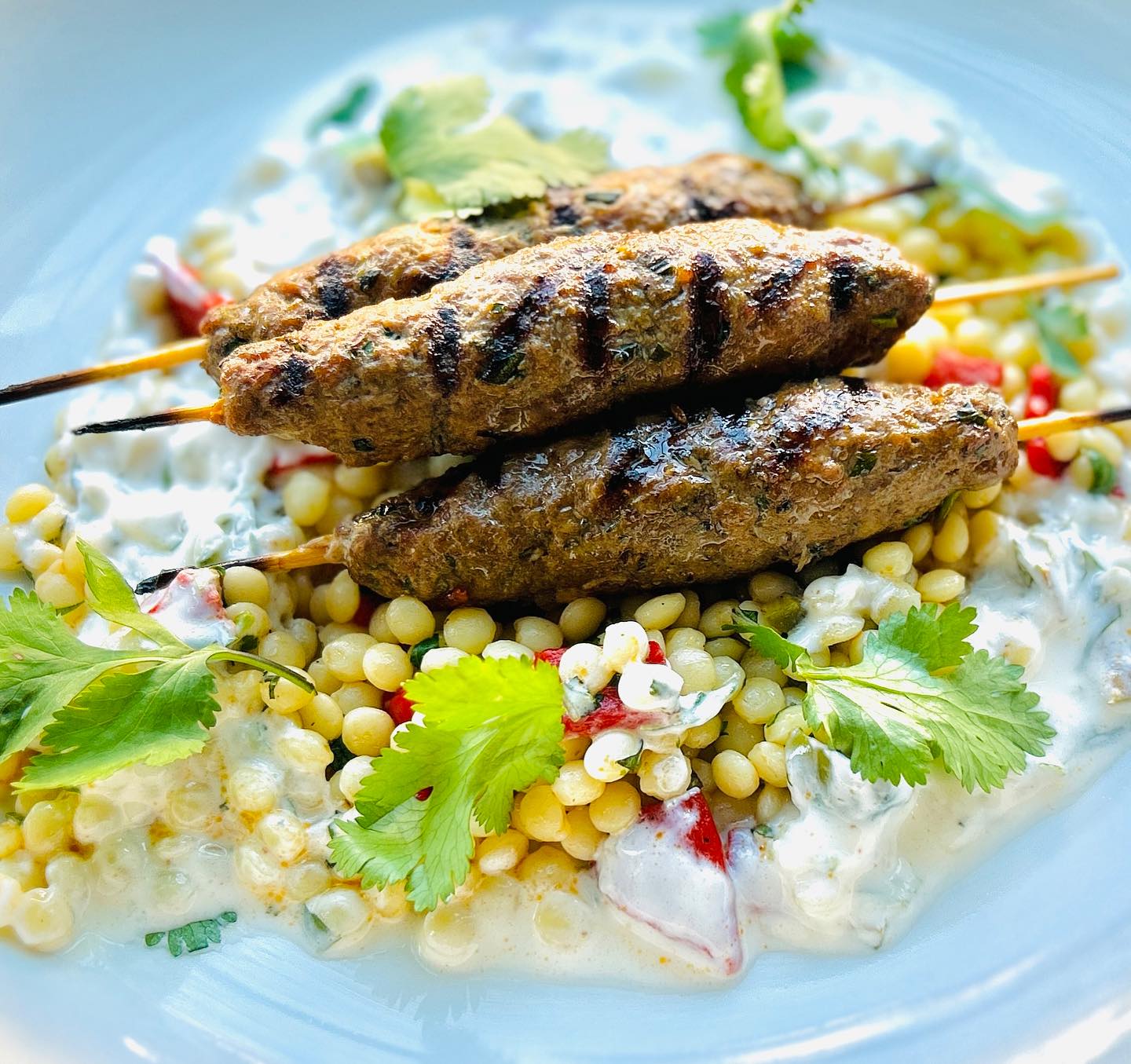 Three grilled skewers on pearl pasta with creamy sauce and herbs.