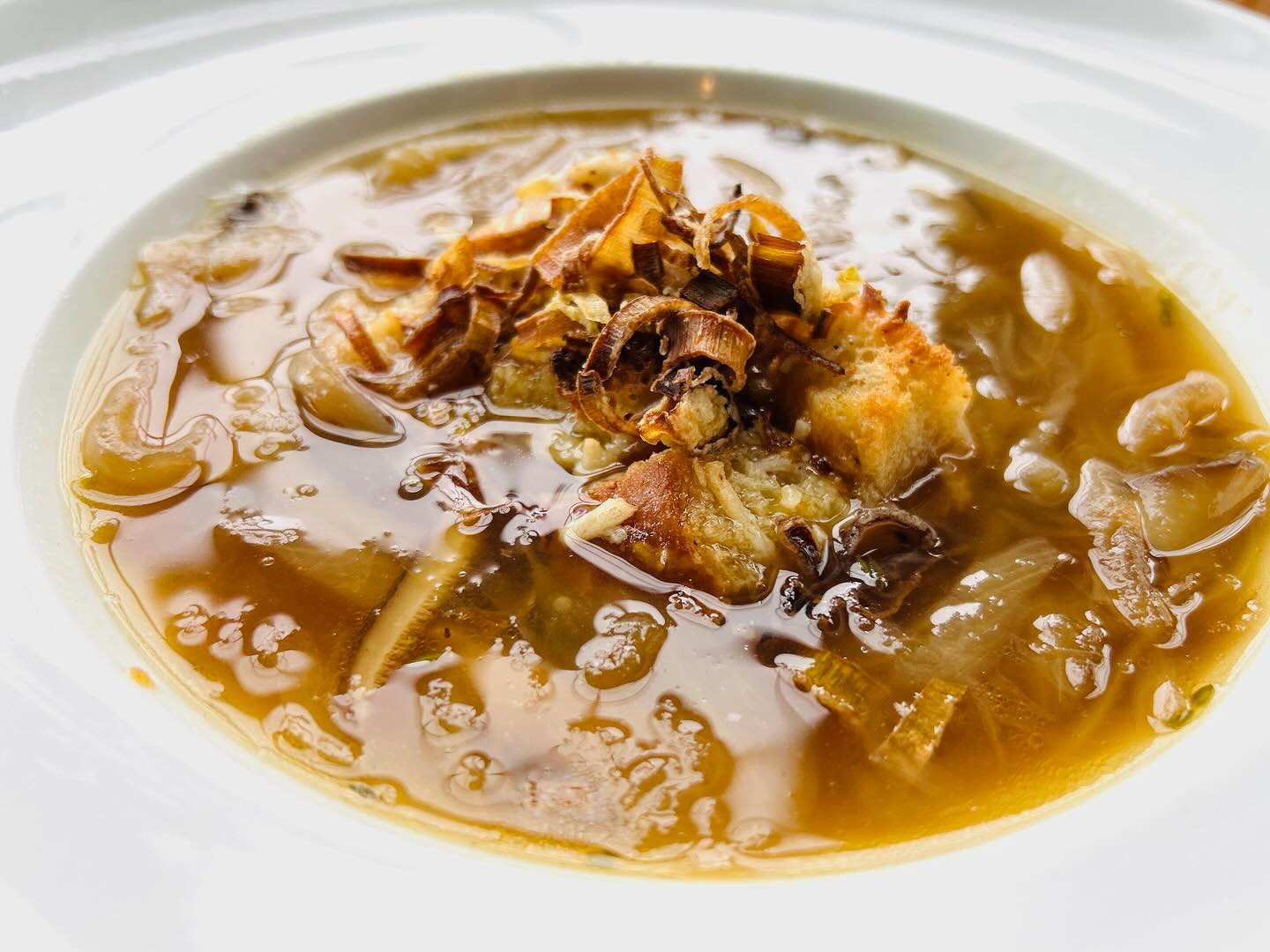 Bowl of onion soup topped with croutons and fried garnish.
