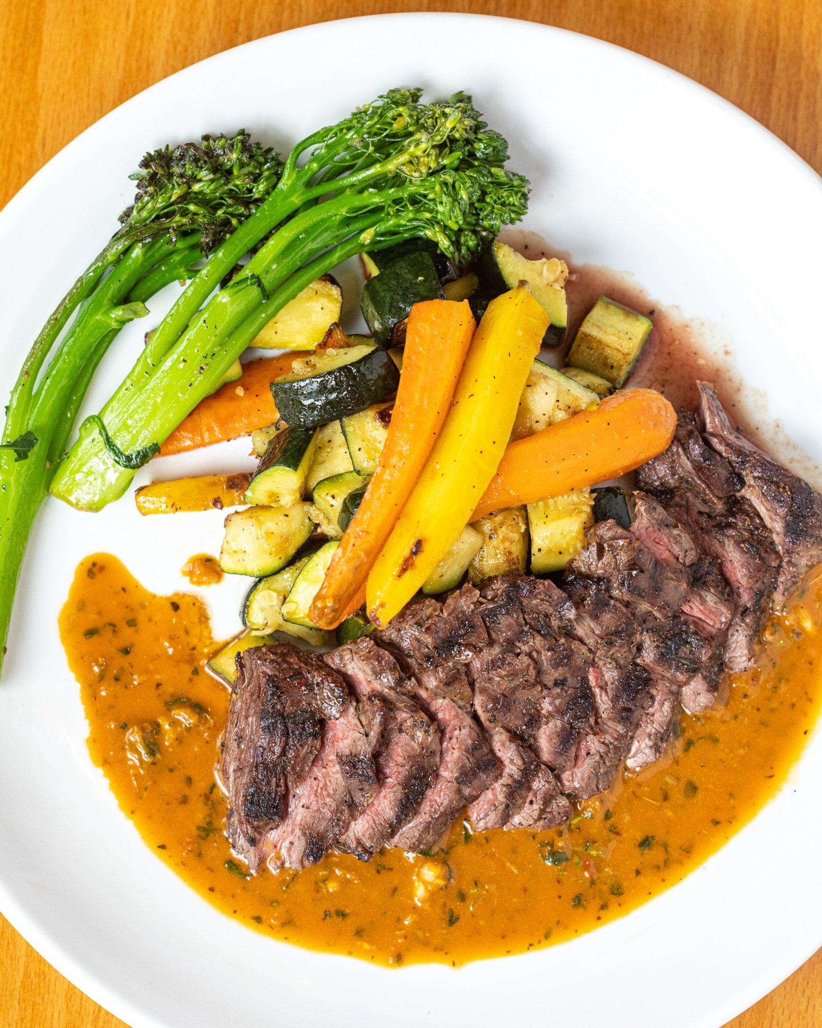 Sliced grilled steak with broccolini, roasted vegetables, and orange sauce.