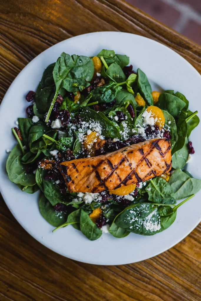 A grilled salmon fillet on a spinach salad with cranberries and cheese.