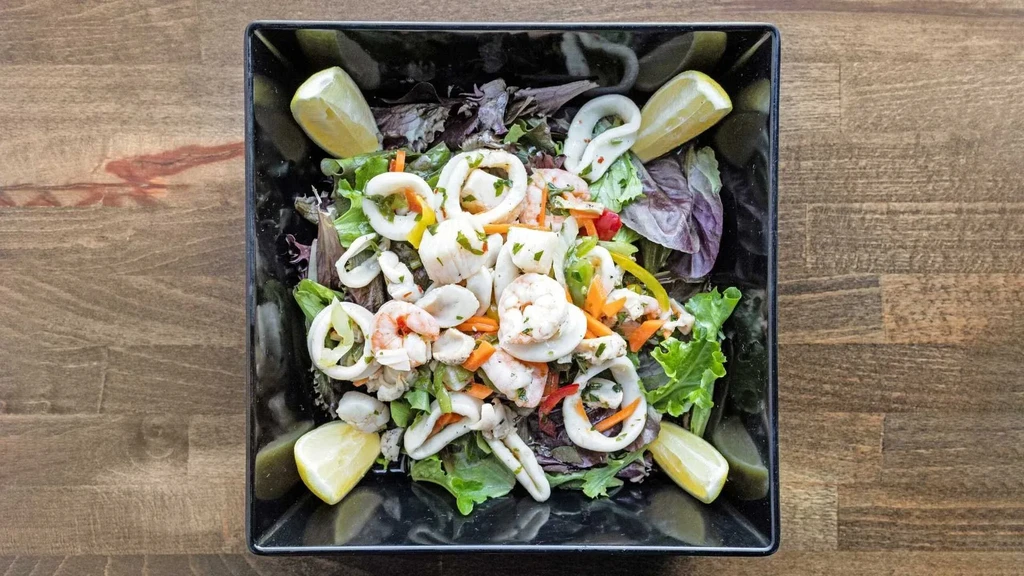 Top-down view of a seafood salad in a black bowl.