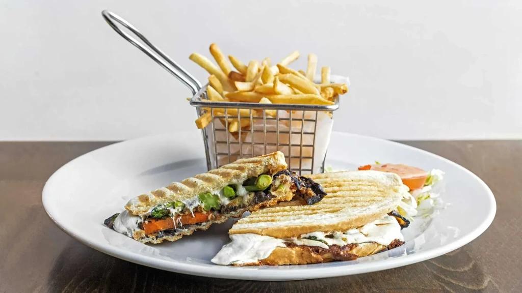 Two panini sandwiches with fries in a basket on a white plate.