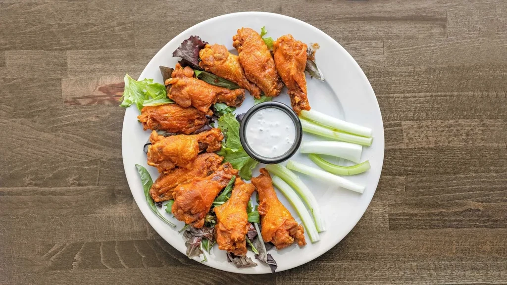 A white plate of buffalo chicken wings, celery sticks, and ranch dip.