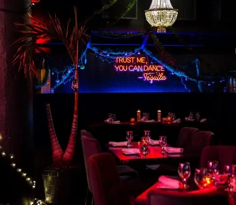 Dimly lit upscale bar interior with glowing neon sign and ornate chandelier.