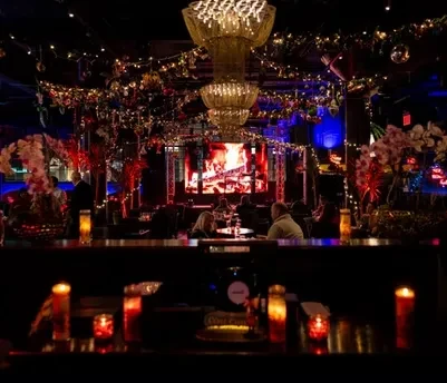 Dim, upscale restaurant interior with chandelier, string lights, and large LED screen.