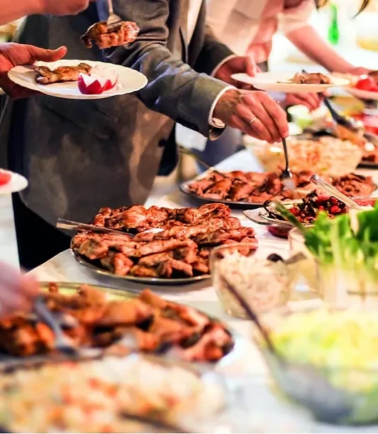 People serving themselves grilled meats and salads at a buffet.