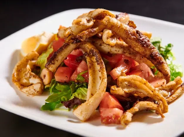 Fried calamari on a bed of lettuce and diced tomatoes.