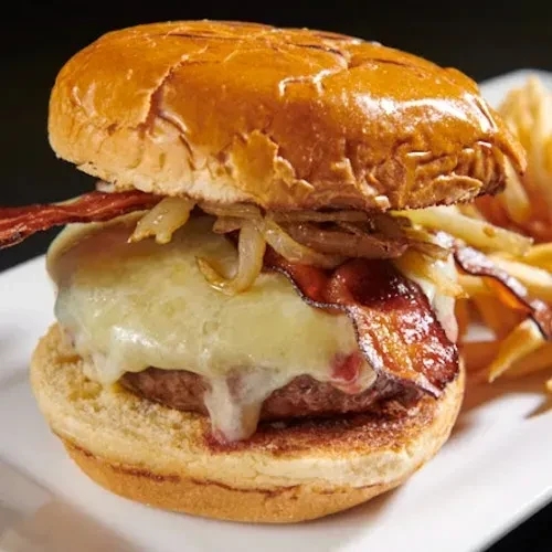 A cheeseburger with melted cheese, bacon, and caramelized onions, with fries.