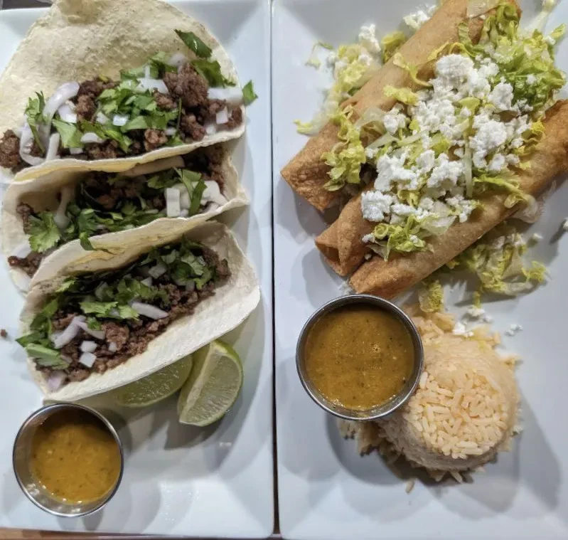 Two plates of tacos, flautas, rice, salsa, and lime slices.