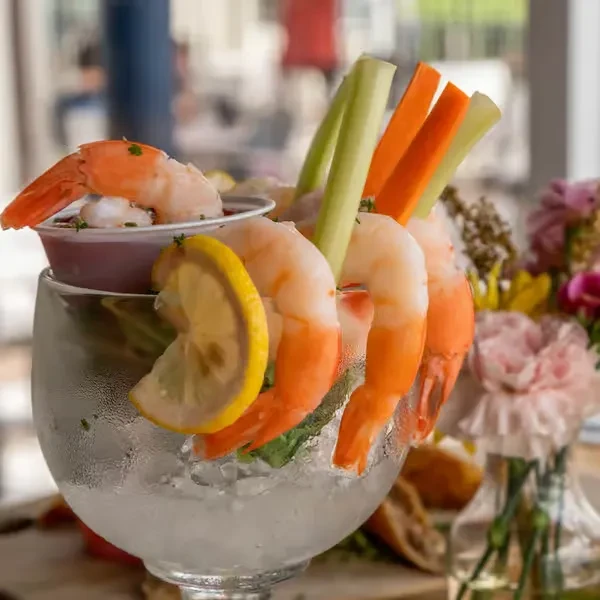 Shrimp cocktail with carrots, celery, and lemon in an iced glass.