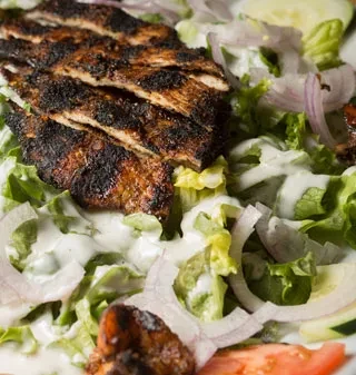 Sliced grilled chicken on a bed of lettuce with dressing.