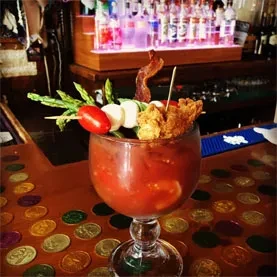 Bloody Mary cocktail in a goblet, topped with bacon and fried chicken.