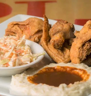 Fried chicken, mashed potatoes with gravy, and coleslaw on a white plate.
