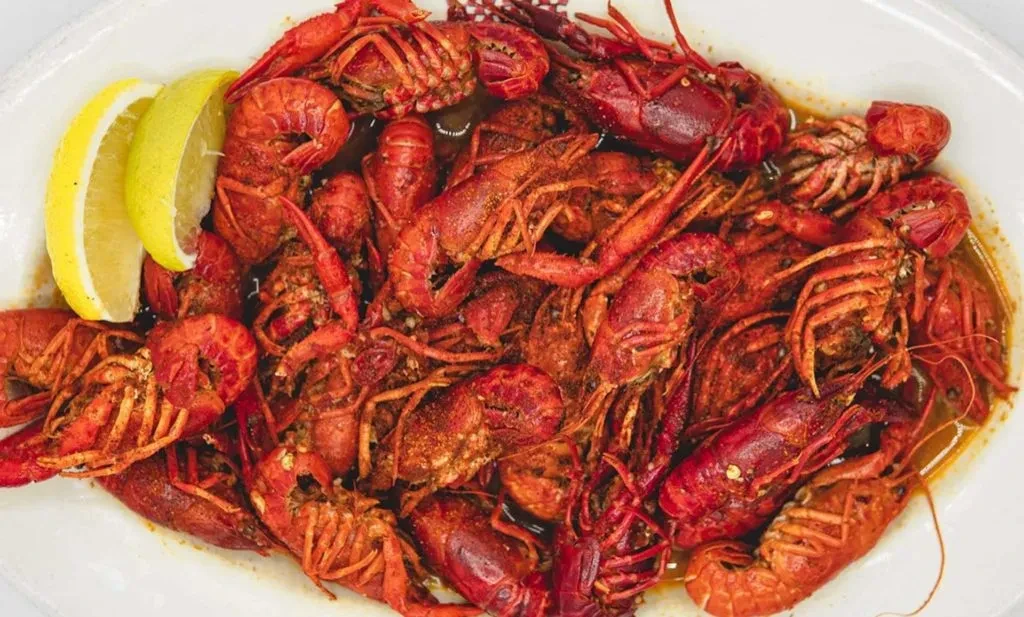 A close-up of a platter of cooked crawfish with two lemon wedges.
