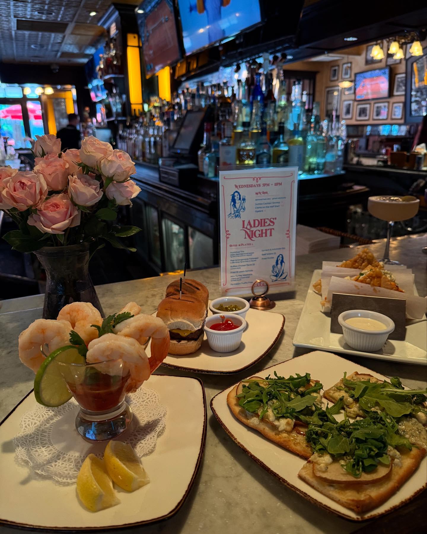 Bar counter with shrimp cocktail, sliders, flatbread, and pink roses.