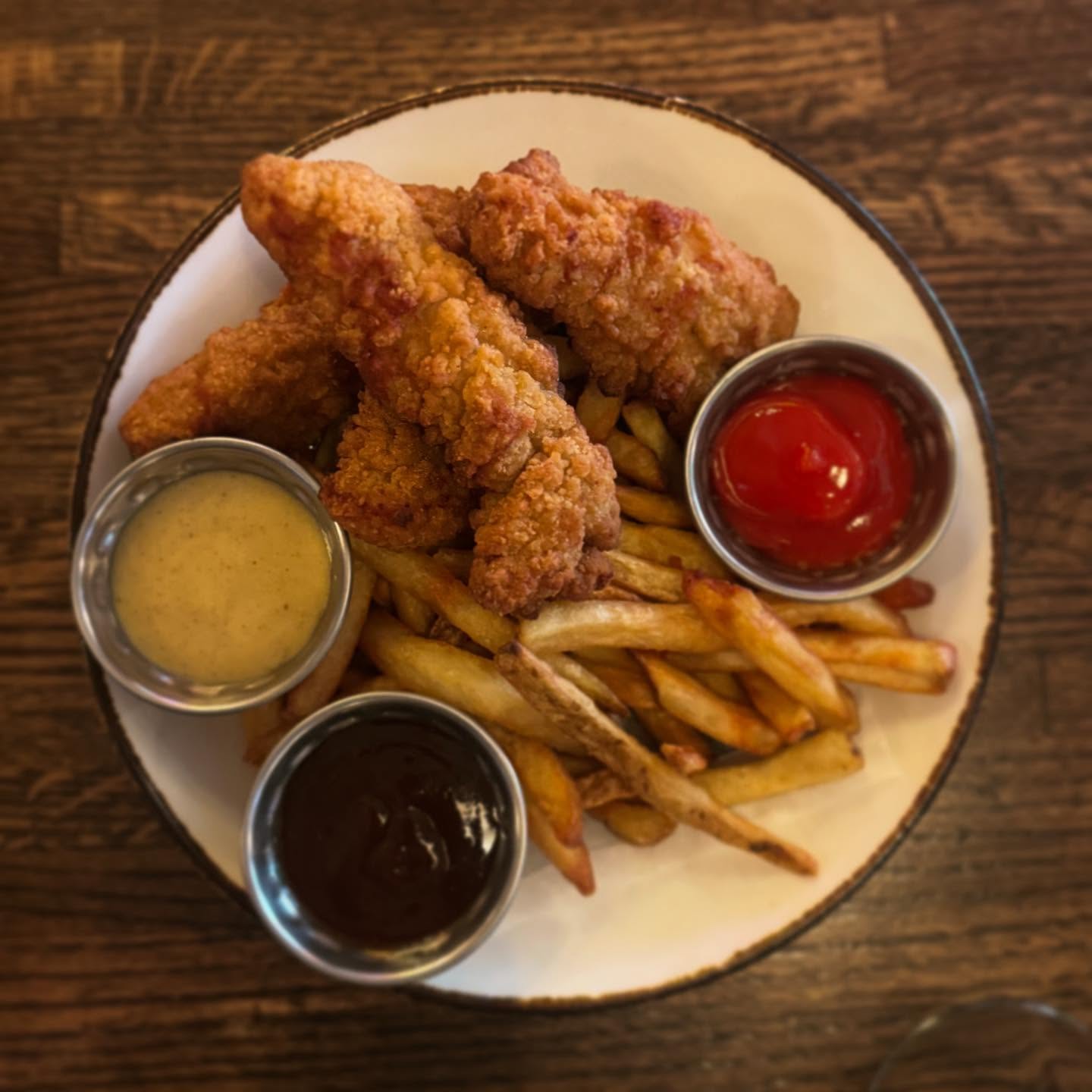 A white plate with chicken tenders, french fries, and three dipping sauces.