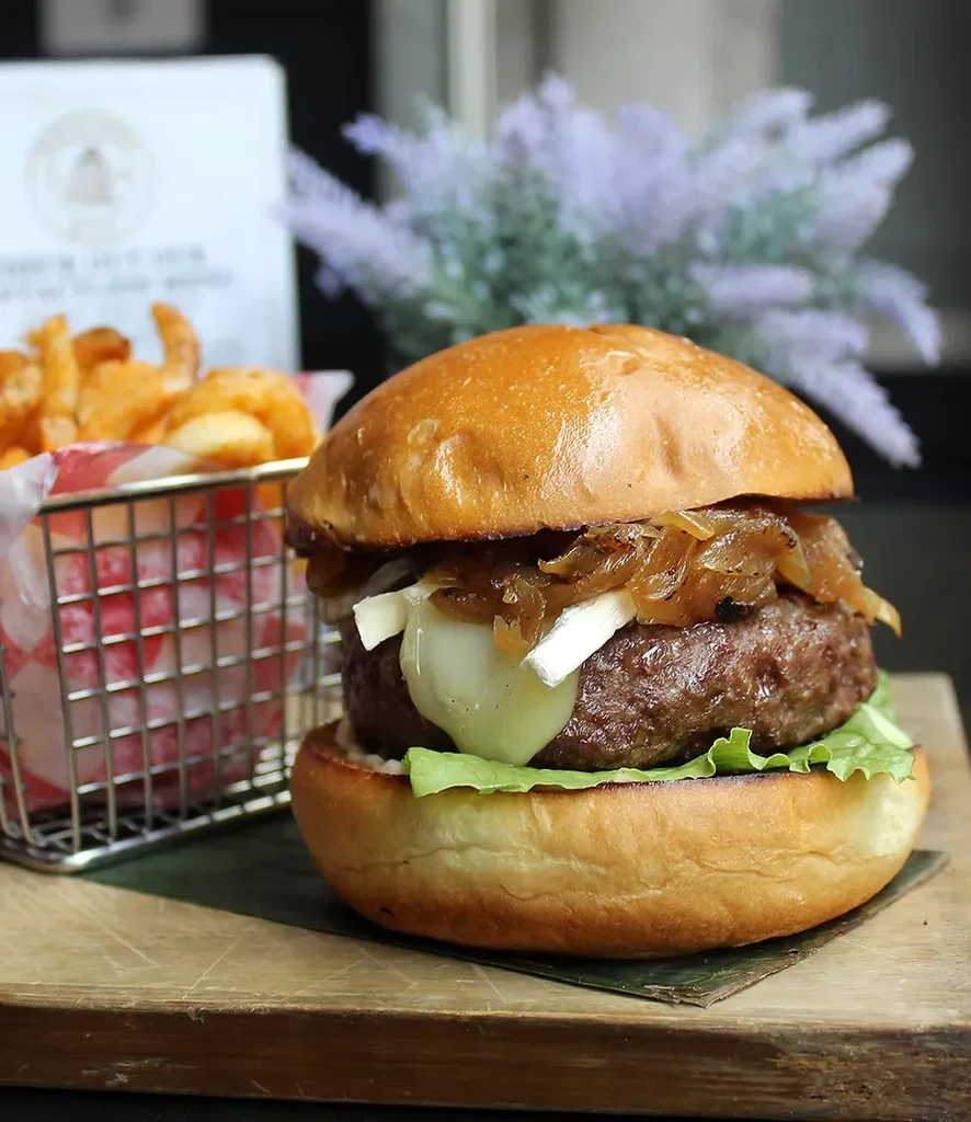 A burger with caramelized onions, cheese, and lettuce, next to fries.