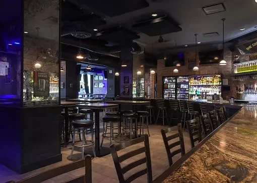 An empty bar with a long bar, bar stools, and tables.