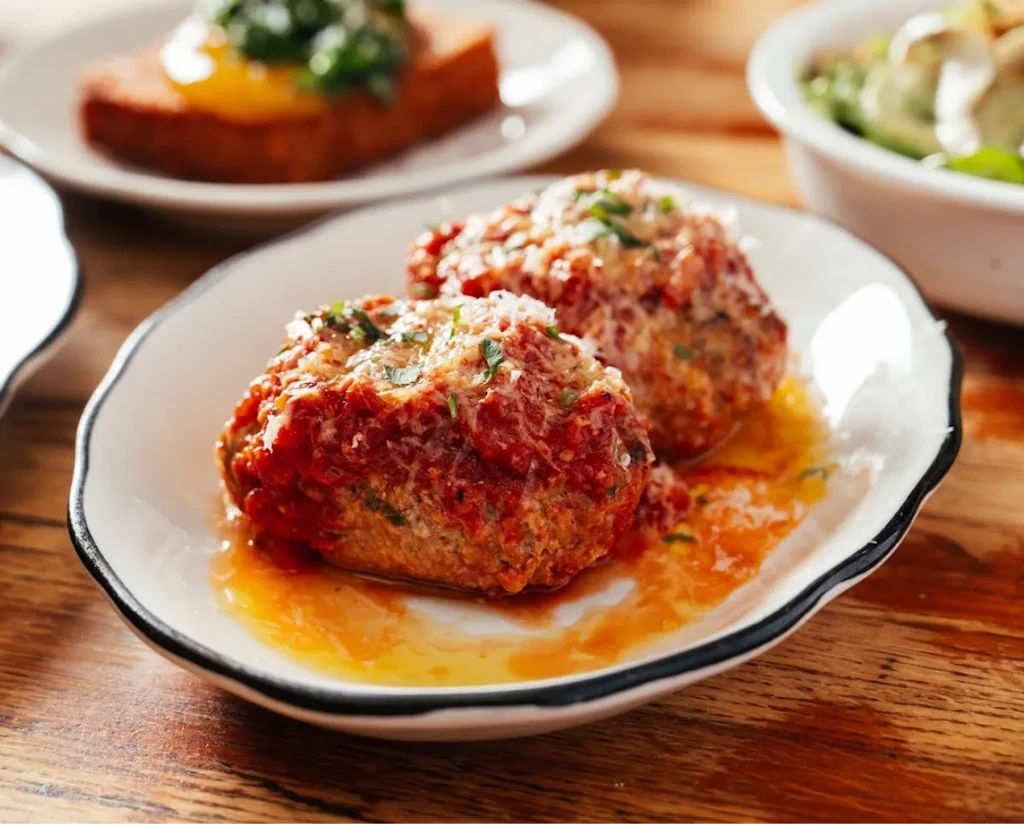 Two large meatballs with sauce, cheese, and parsley on a white plate.