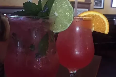 Two pink cocktails garnished with lime, mint, and orange slices.