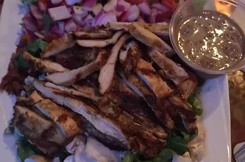 Grilled chicken strips over salad with a side of dressing.