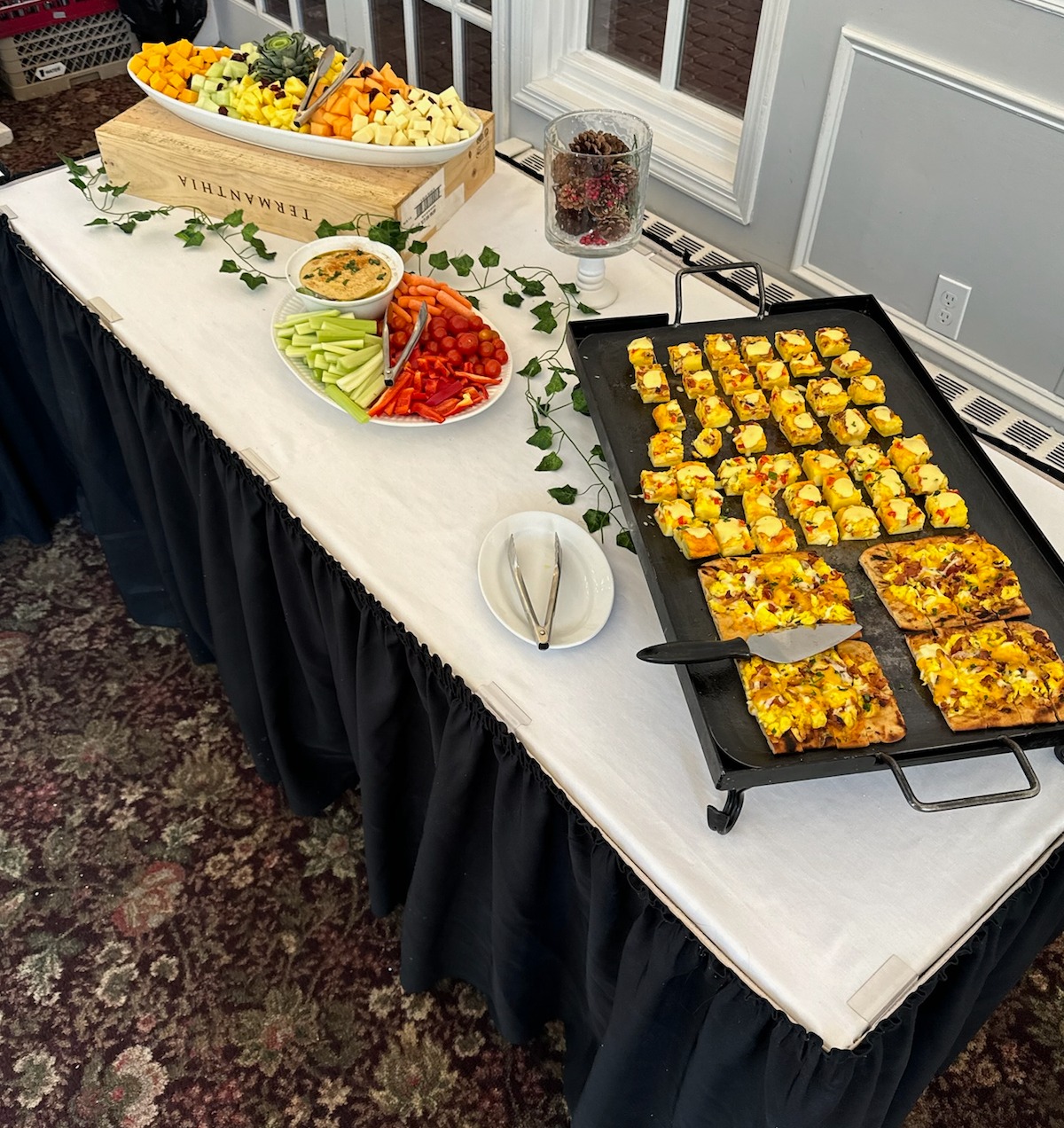 Buffet table with platters of fruit, vegetables, and hot appetizers.