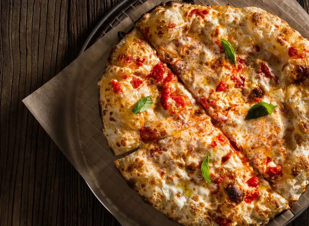 Round, cheesy pizza with red sauce and basil, on a dark wooden table.