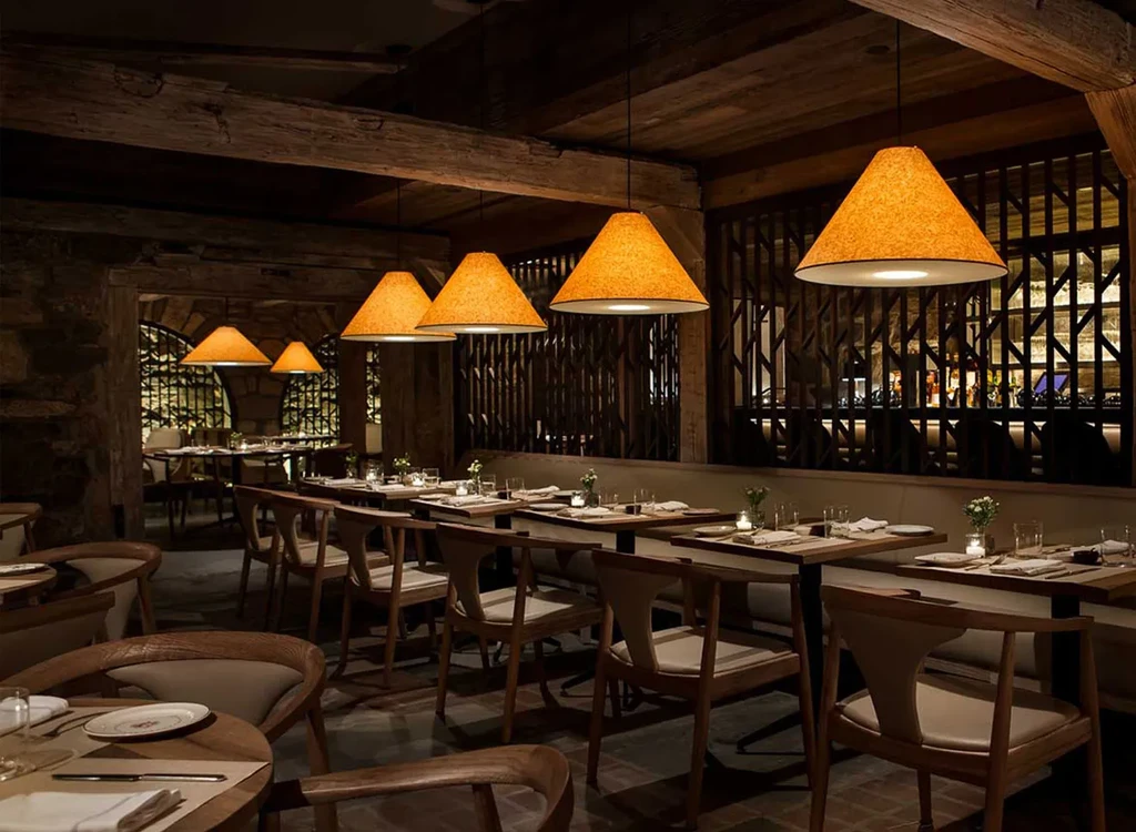 Rustic restaurant with warm lighting, wooden beams, and elegant dining tables.