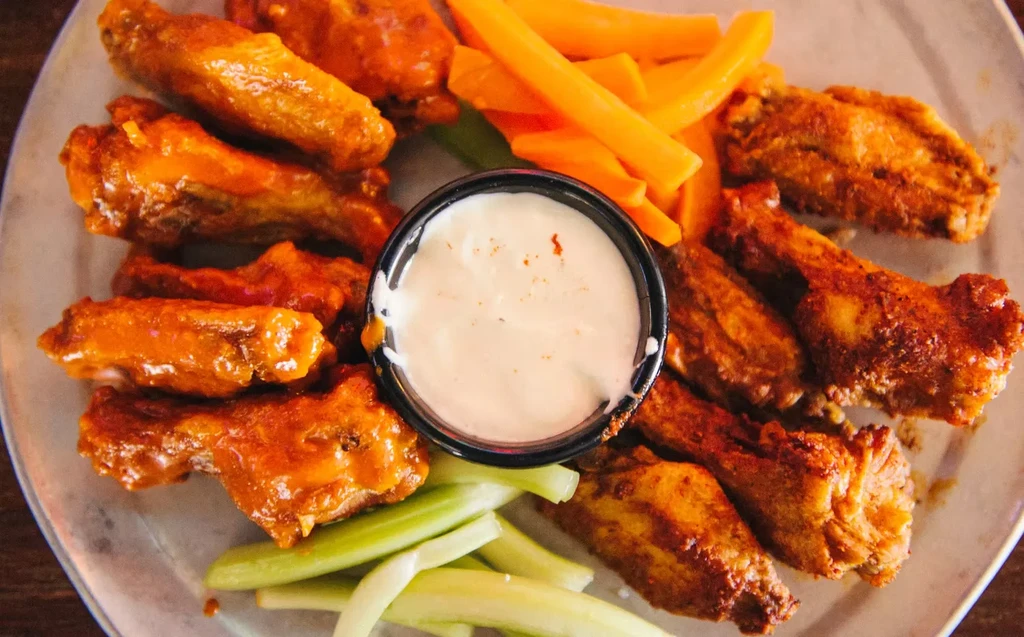 A plate of chicken wings, celery sticks, carrot sticks, and ranch.