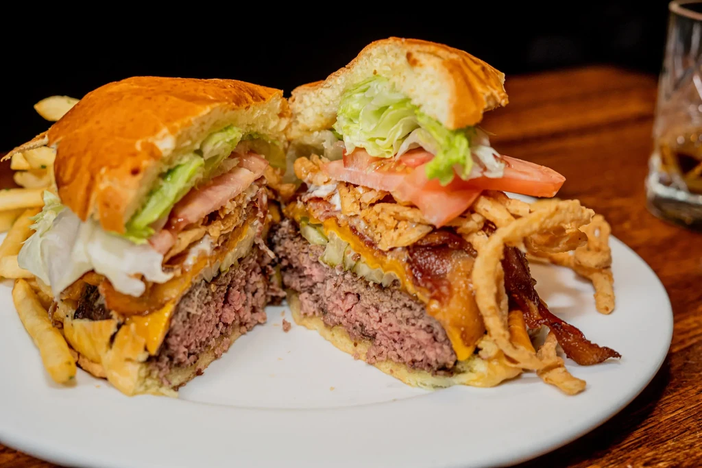 A large burger cut in half, revealing its medium-rare patty and toppings.