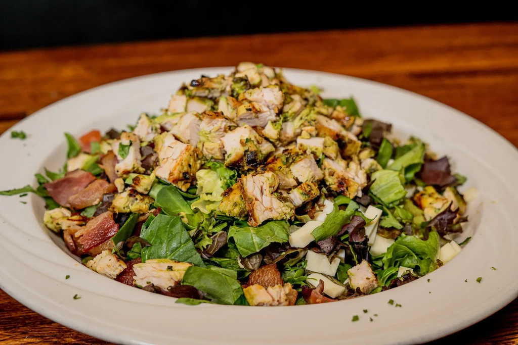 A large white plate of grilled chicken salad on a wooden table.