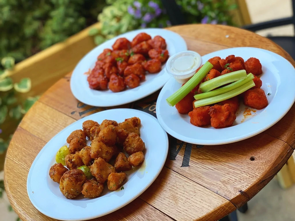 Three plates of appetizers are on a round wooden table outdoors.