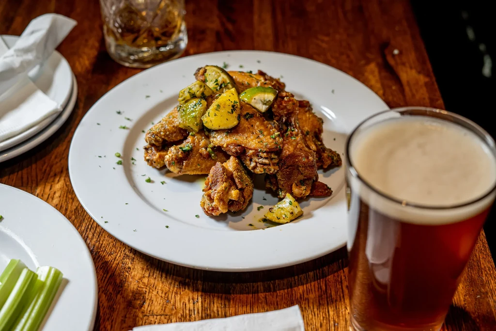Fried chicken wings with lime and a glass of beer on a wooden table.
