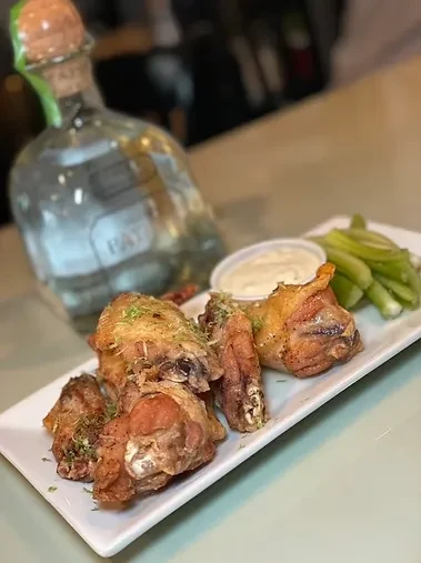 Chicken wings, celery sticks, and dip on a plate with a tequila bottle.