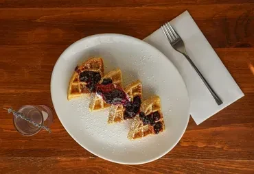 Three waffle sections topped with blueberries and powdered sugar on a white plate.