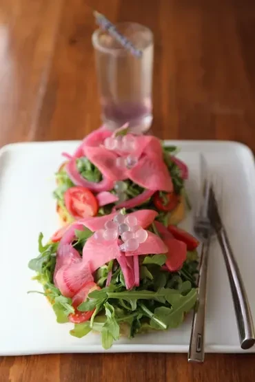 Two avocado toasts topped with arugula, radishes, onions, and caviar.