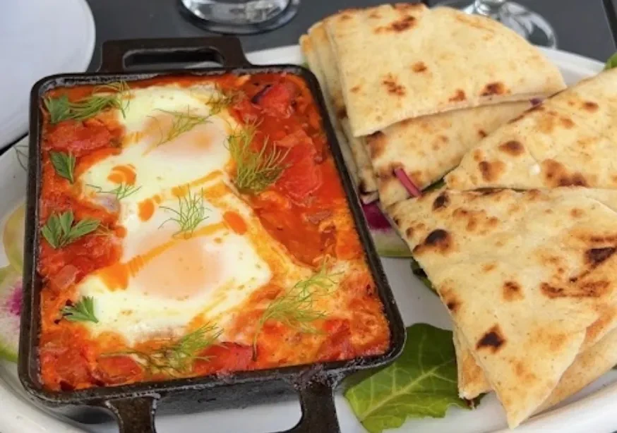 Shakshuka with three eggs, garnished with dill, and pita bread.