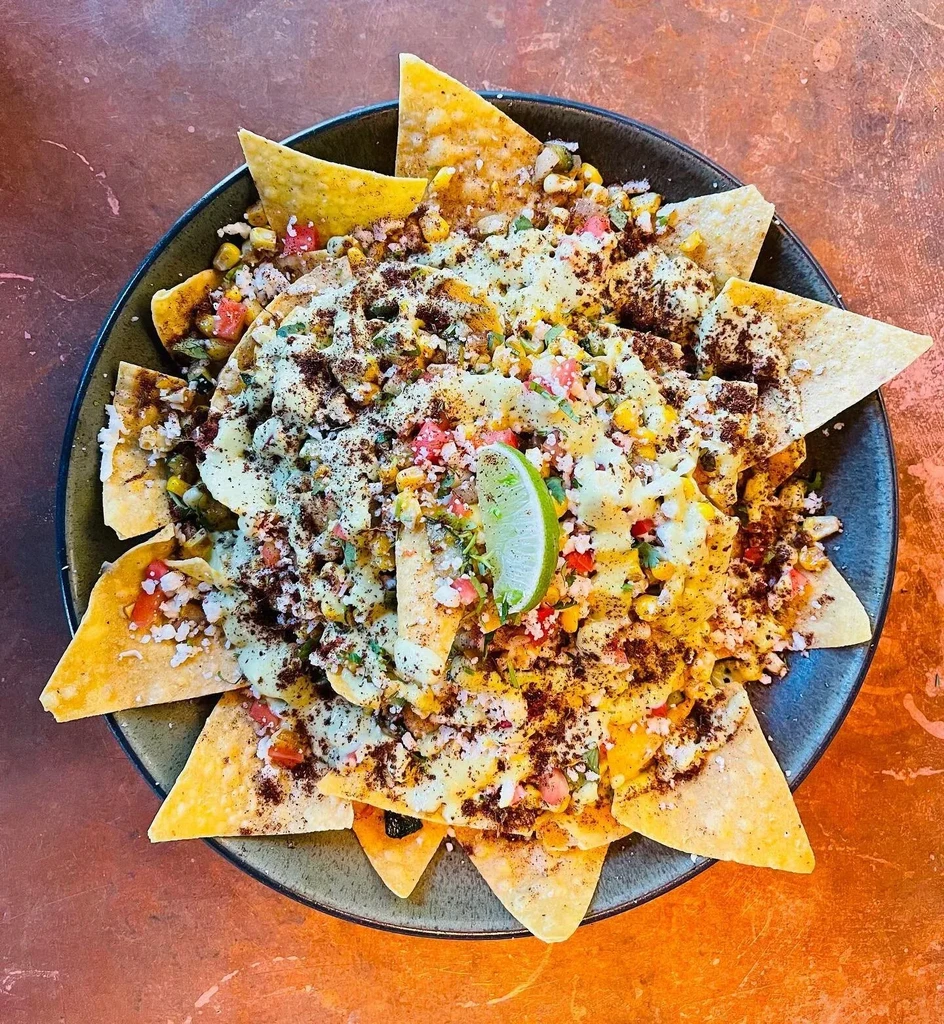 Nachos with corn, cheese, cilantro, spices, and a lime wedge.