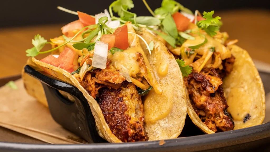 Two corn shell tacos with meat, cheese, tomatoes, and cilantro.