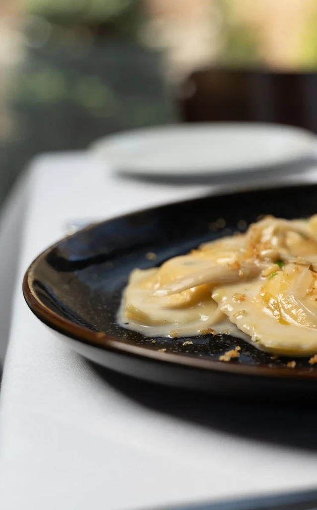 Ravioli in a creamy sauce with garnish on a dark plate.