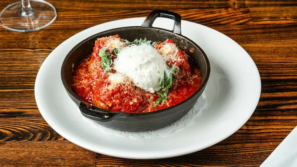 Meatballs in a skillet with red sauce, creamy cheese, and basil.